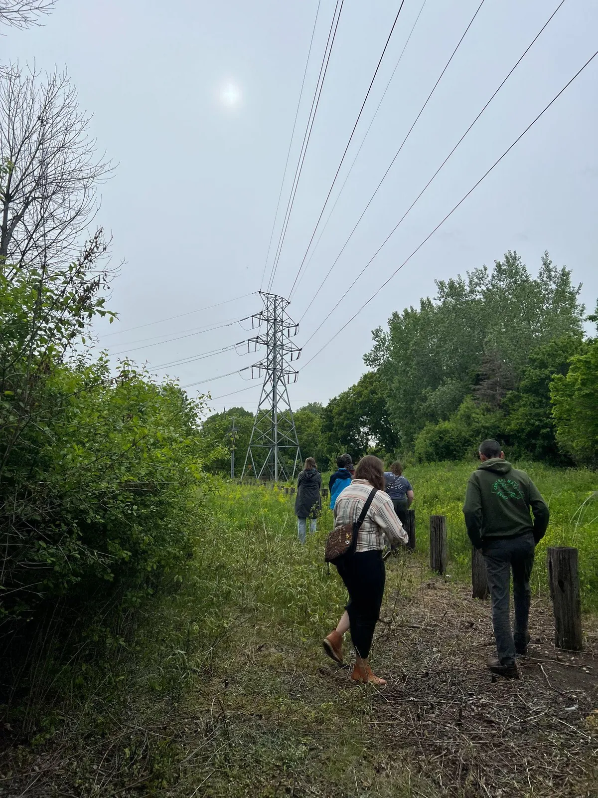A group walking single file along the edge of the lot beneath transmission towers